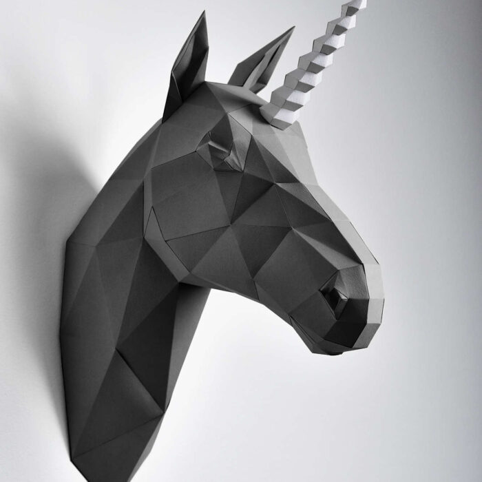 Graphitic black unicorn hanging on white wall with grey shadows. Horse has intresting geometrical shape and straight lines. Horse's head made grom paper. Original decoration for modern design.